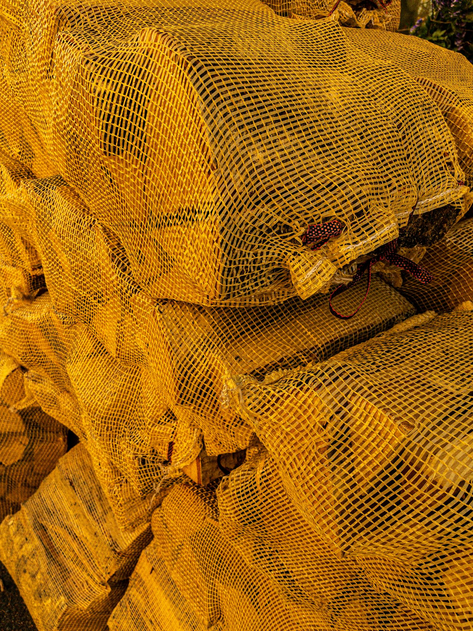 Piled yellow net bags containing firewood, ideal for outdoor heating.